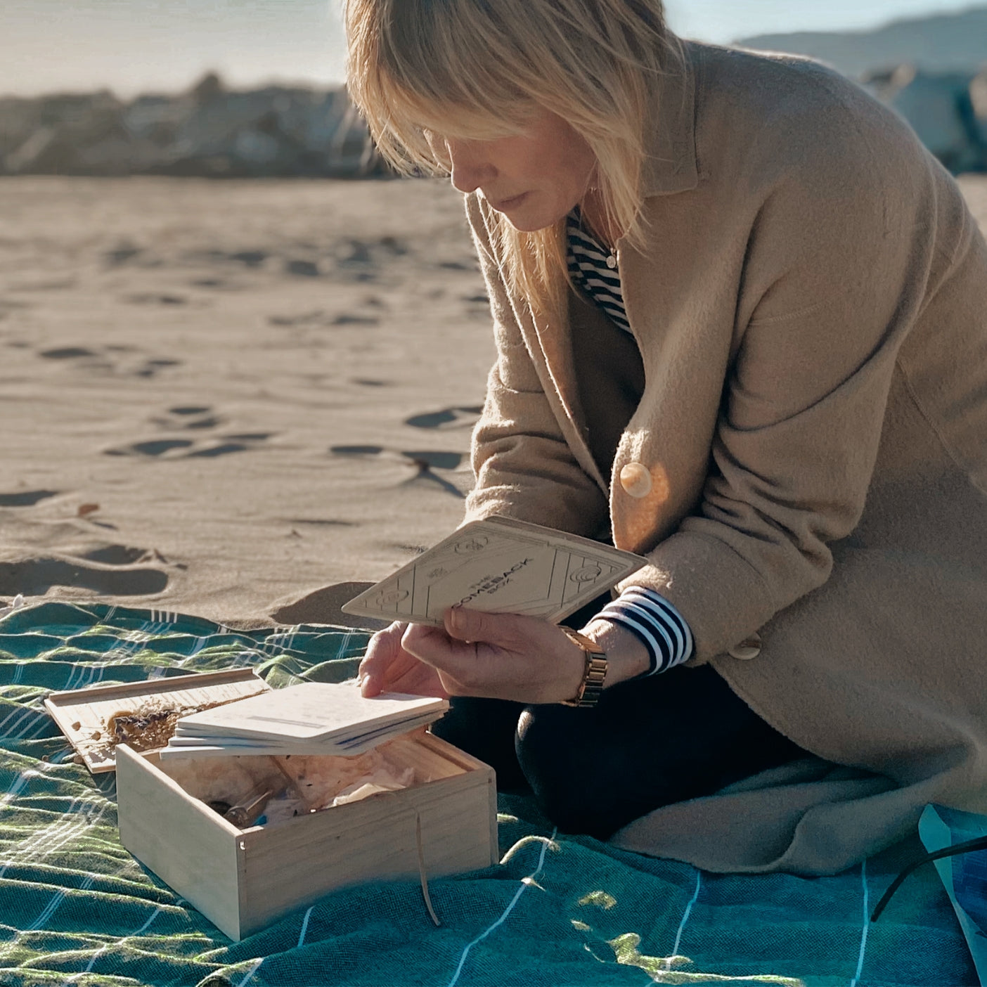 The Comeback Box: woman opening the wooden box on a beach in the sun.