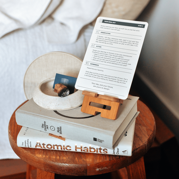 The Vision Box: Bedside table with books stacked and an instruction card sitting in a card holder.