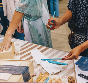 Woman holding a pen and writing on pieces of paper. The Box Co wooden box on a table with thoughtfully curated items.