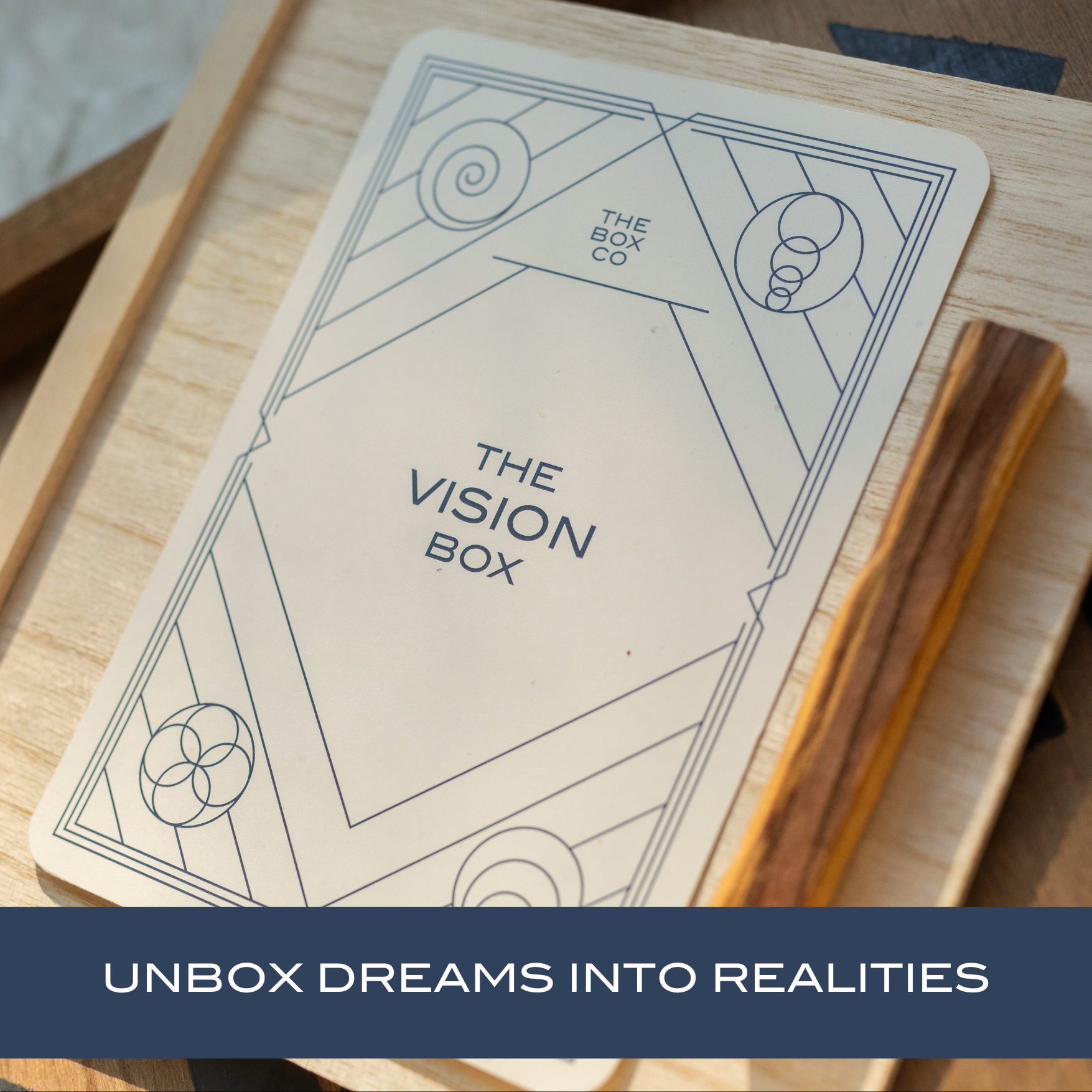 The Vision Box: card on a wooden box next to palo santo stick. Text overlay "UNBOX DREAMS INTO REALITIES".