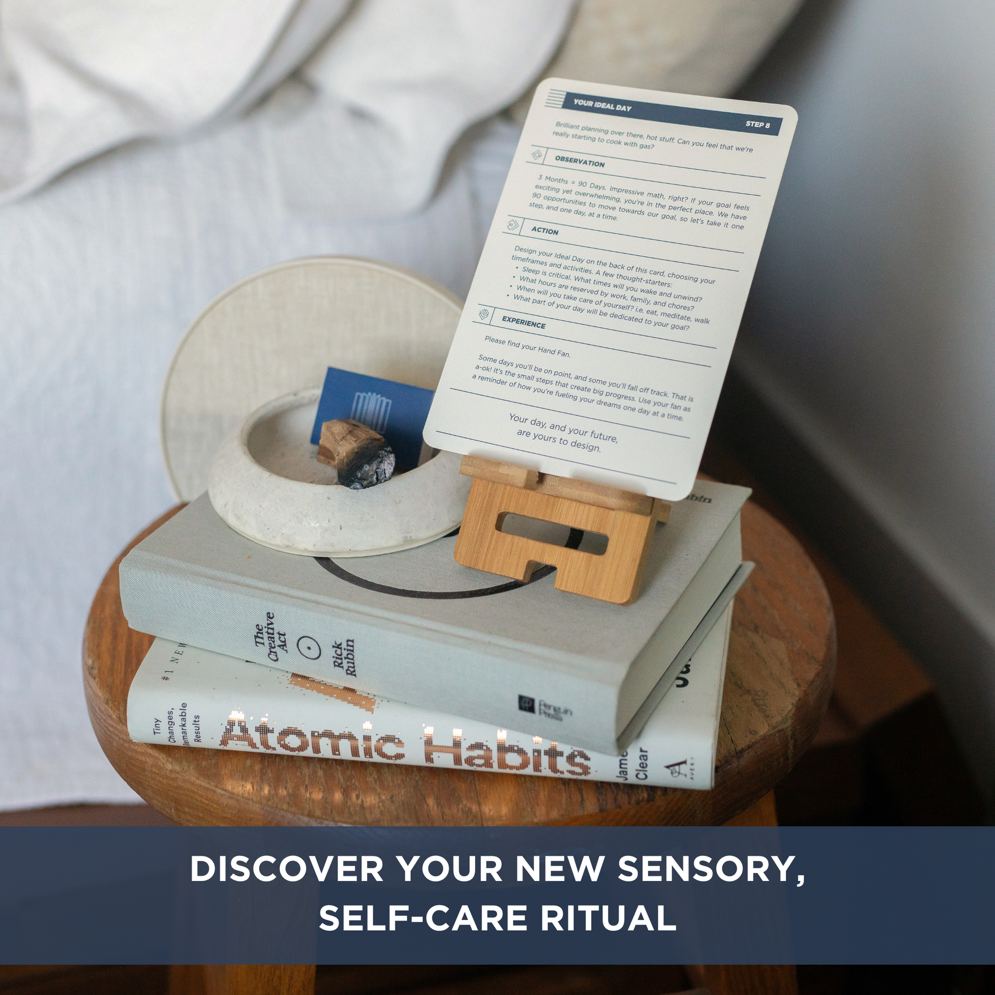 The Vision Box: Bedside table with books stacked and an instruction card sitting in a card holder. 